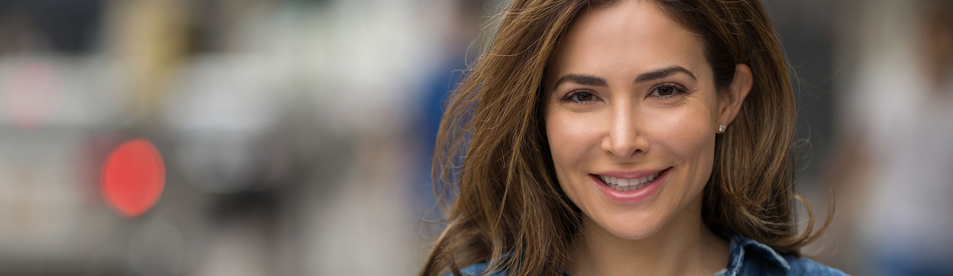 Woman with long hair smiling at camera, standing outdoors during daytime.