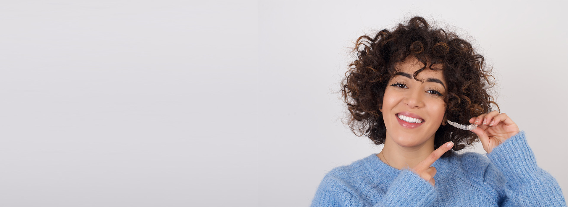 A woman with curly hair smiling at the camera, wearing a blue top and holding a phone to her ear.