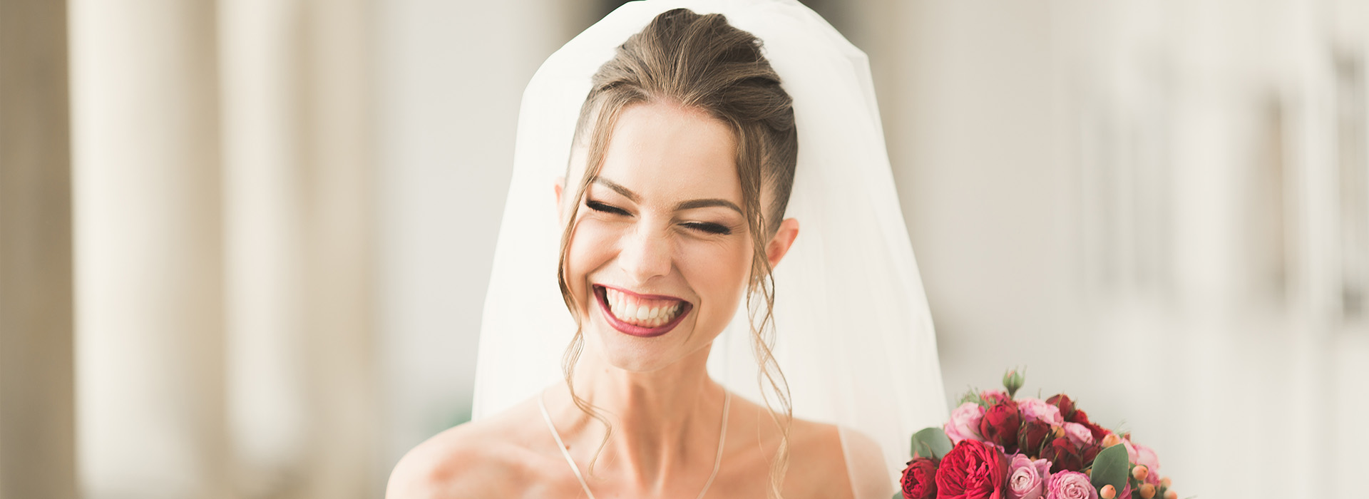 The image features a bride wearing a white wedding dress and veil, smiling at the camera with joy and celebration, captured during a wedding ceremony.