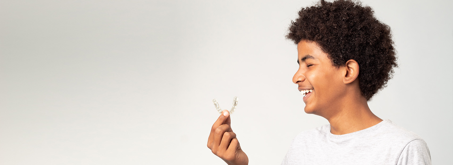 A young boy with curly hair, smiling at the camera while holding a small object in his hand.