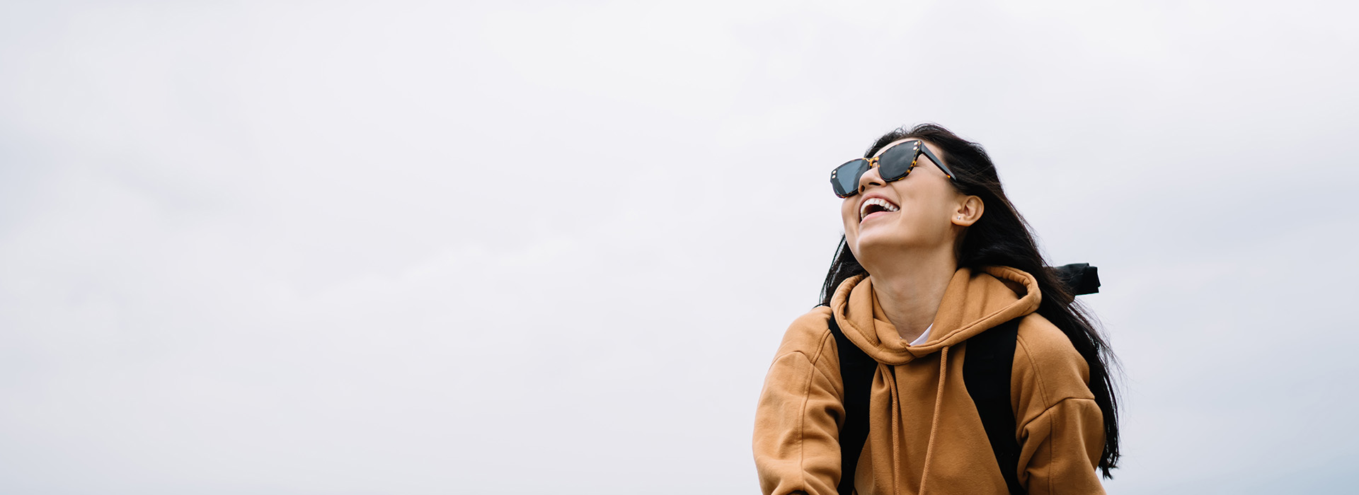 A person in a hoodie stands against a sky background, smiling with sunglasses on their head.