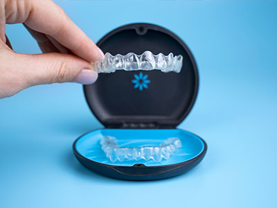 The image shows a person s hand holding an open dental impression tray with a blue background, displaying a set of clear dental impression trays.
