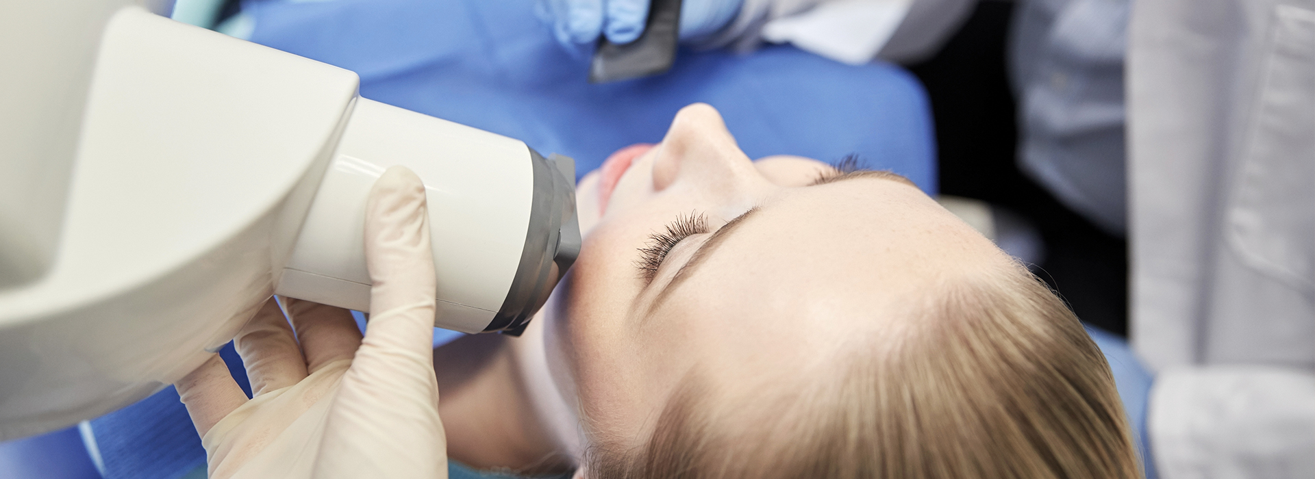 A woman receiving dental care, with a dental practitioner using a magnifying glass and holding a mirror to examine her teeth.