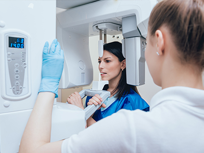 A woman in blue scrubs is inspecting a large white 3D scanner with the help of another person, possibly in a medical or dental setting.
