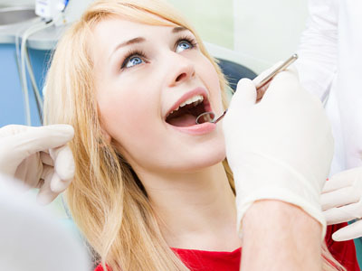 A woman receiving dental care with a dentist performing an examination while wearing gloves and a mask.