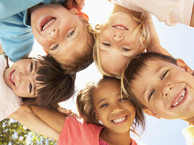A group of children standing together with smiles on their faces, under a bright sky.