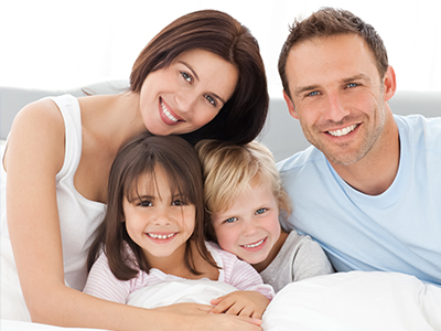 A family of four, including two adults and two children, are smiling and posing for a photograph together on a bed.